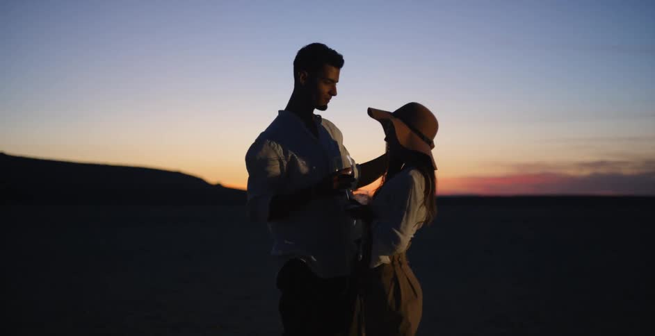 A man and woman dance while drinking wine at dusk