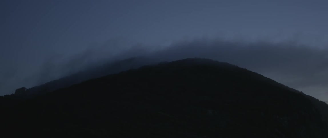 Clouds float over a hill at night