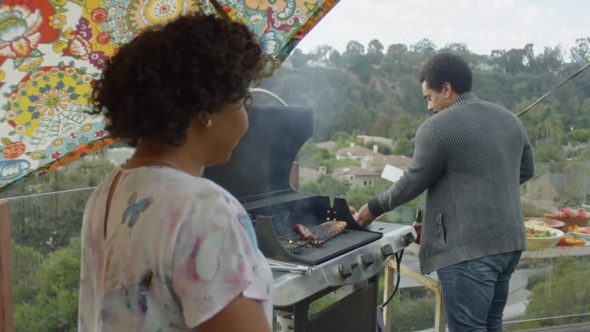 Woman stands near man who is barbecuing on cloudy day