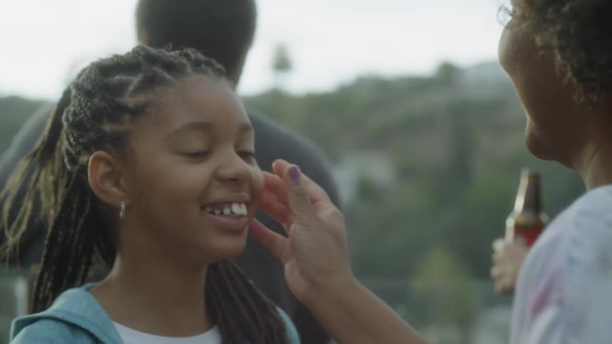 A woman brushes something off a girls face as they smile and talk