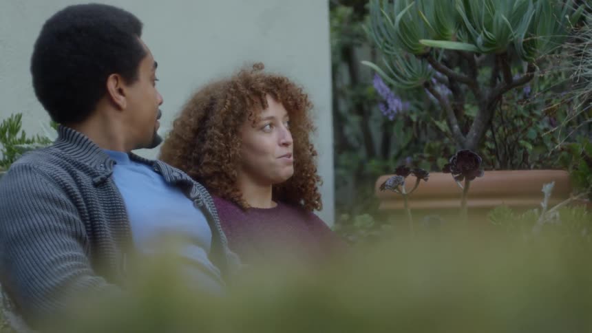 A man and woman sit next to each other in a garden and talk