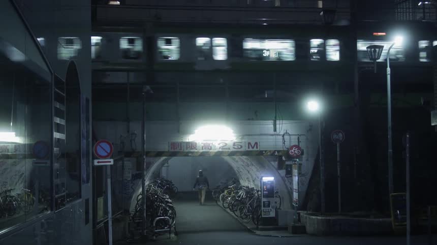 Person walks in a tunnel with a train passing overhead at night