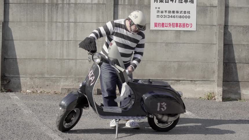 Man wearing a striped shirt wipes off a small motor bike