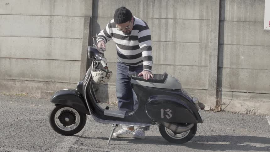 A man leans over a parked scooter