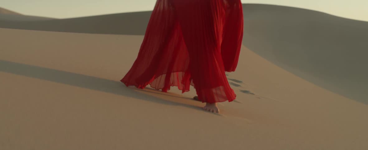Woman in flowing red dress walks across desert