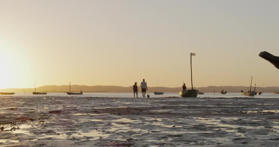 People stand near a boat on a lakeshore at sunset