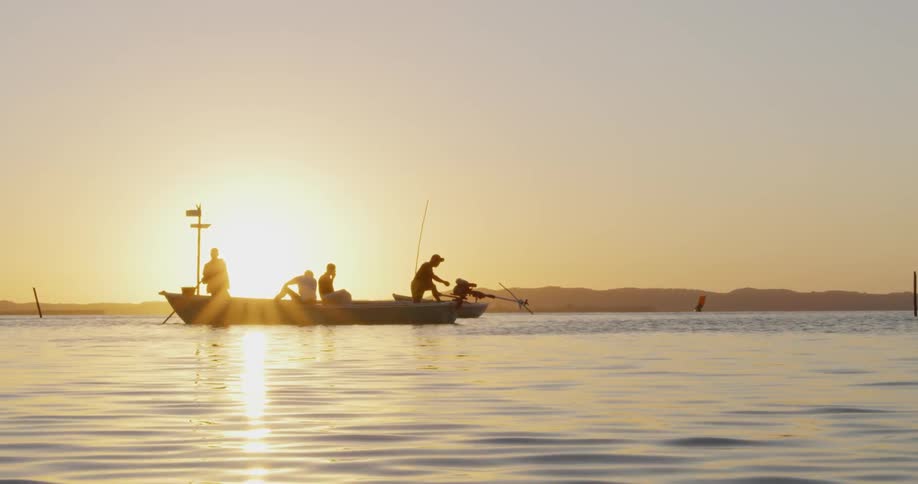 The sun sets as people fish on a calm lake