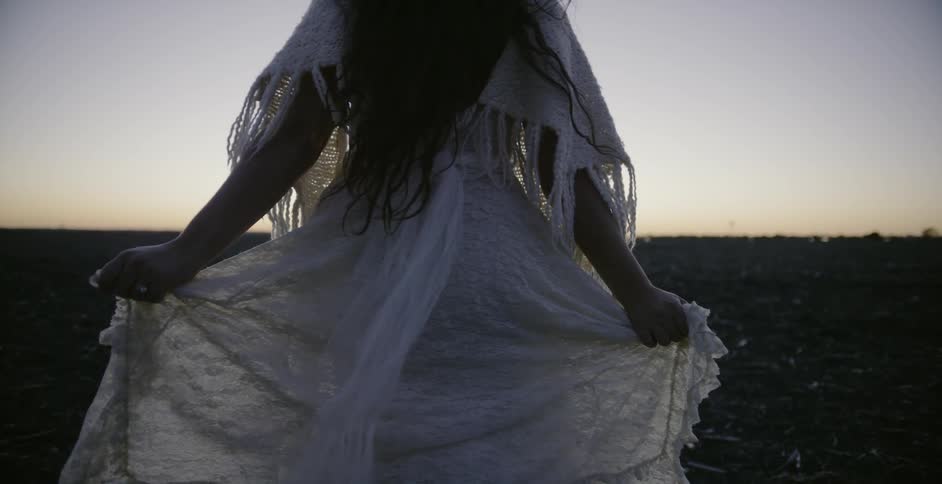 A woman holds the skirt of her dress out as she skips ahead at sunset
