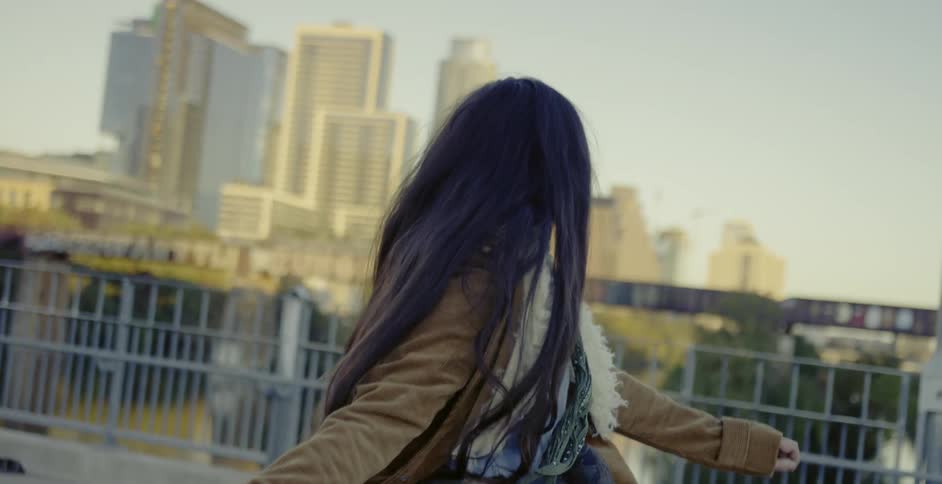A woman is dancing and spinning on a walkway overlooking a city during the daytime