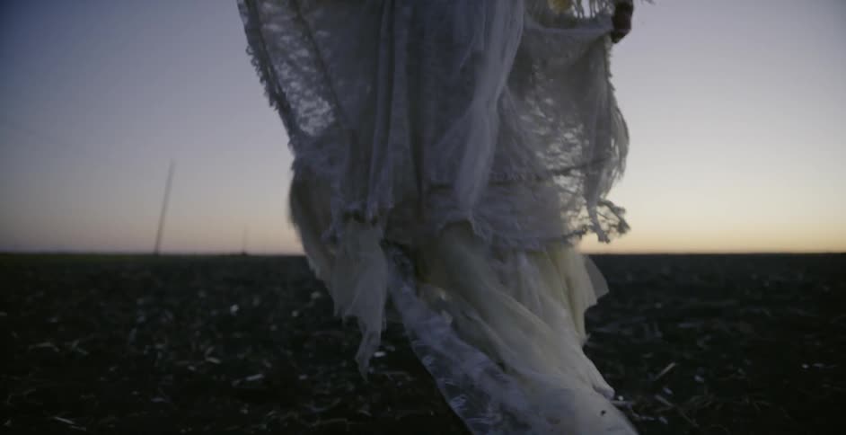 Woman in flowing white dress run across a field of dirt