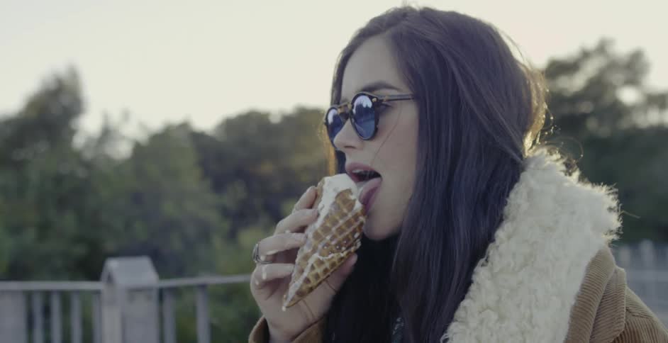 A woman eats a melting ice cream cone outside