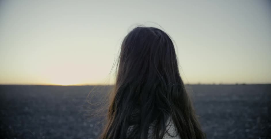A woman stands in a rural field at sunset