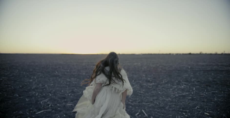 Woman smiles then turns and runs away across an empty field of dirt