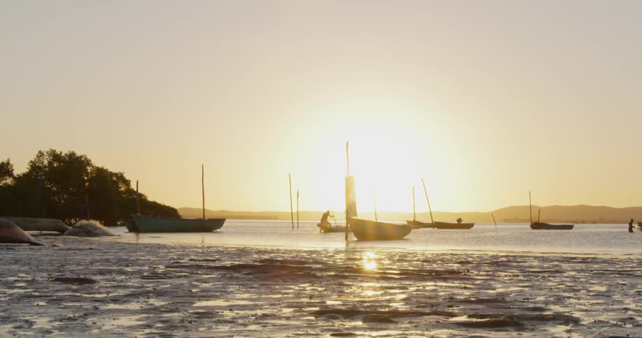 Small boats are anchored in shallow water at sunset