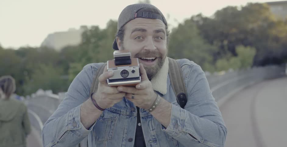 A man is smiling as he starts to take a photo outside in daylight