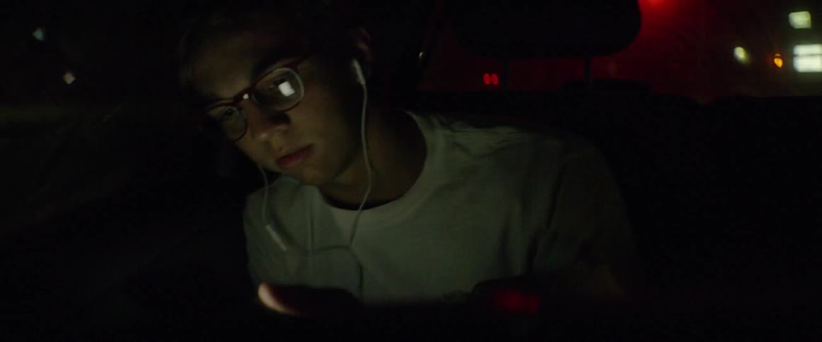 Boy rides in car listening to headphones and writing in journal at night