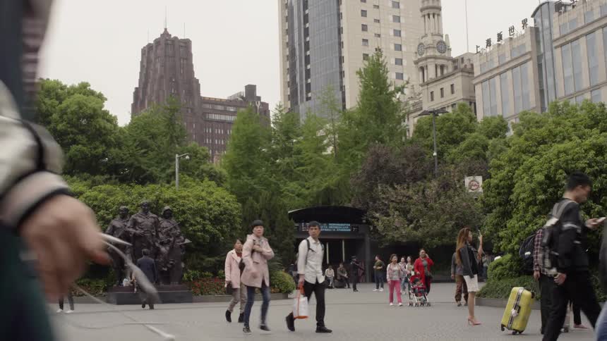 People walk past statues and trees in a city public garden