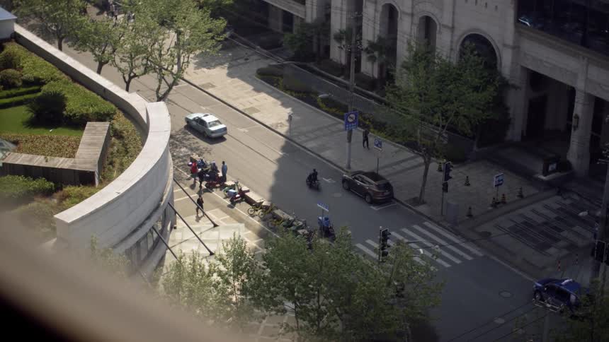 People stand outside near an intersection while cars and motor scooters drive by
