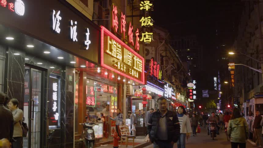 People enter stores and restaurants on a city walk at night