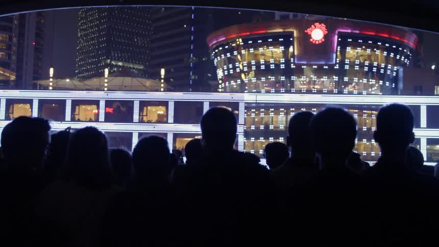 People on shore film a dinner cruise ship go by at night