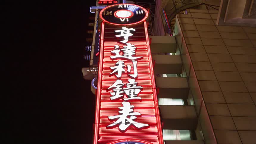 A neon sign on a building in an asian city is flashing at night