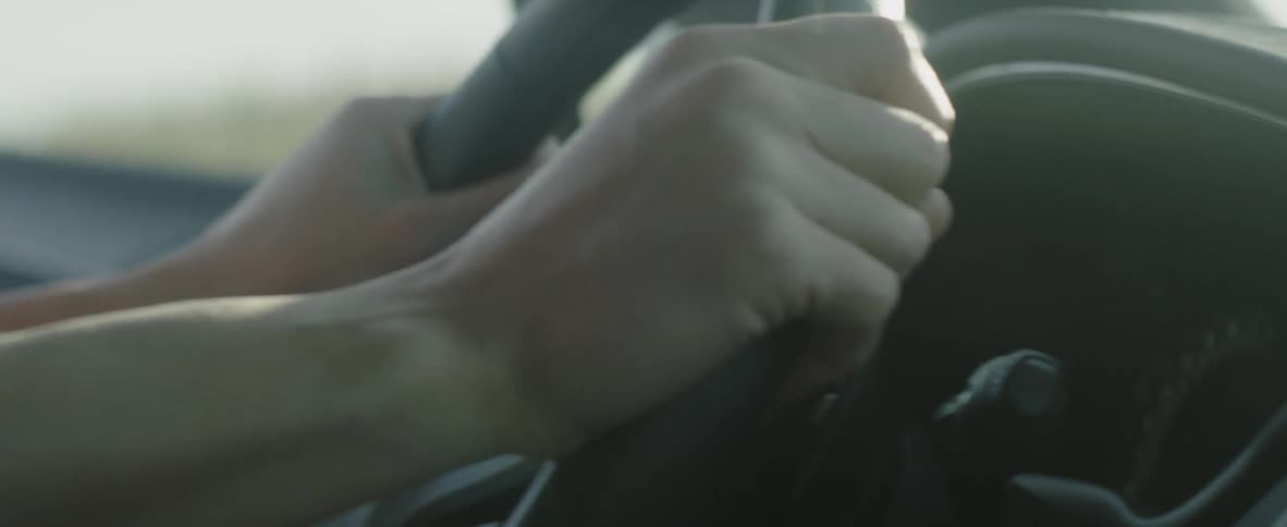 A man is placing his hands on a car's steering wheel in daylight