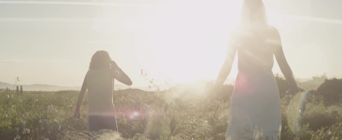 A woman and girl are walking through a field with flowers in daylight