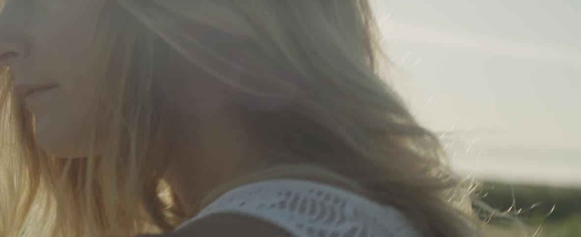 A woman standing outside in the sunlight is turning her head