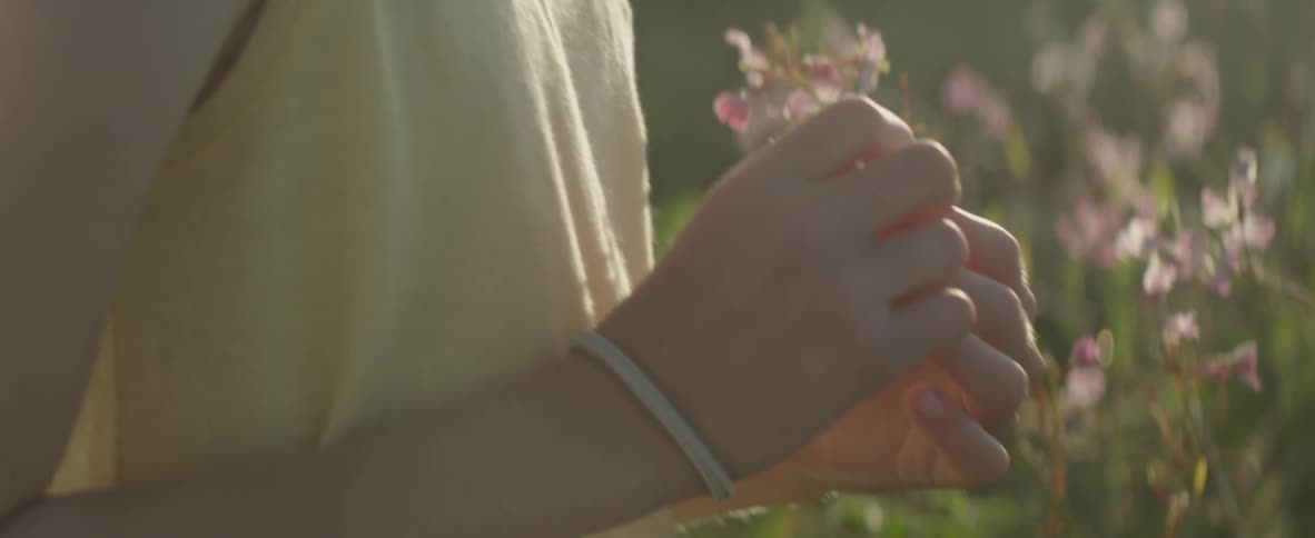 A woman holds a small wild flower outside on a sunny day