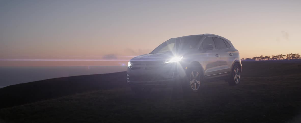 SUV sitting idle headlights beaming in natural setting at dusk