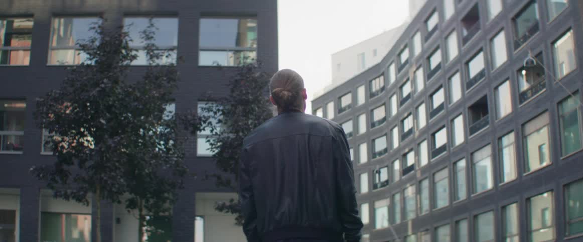 A man stands alone on an urban pathway admiring contemporary multi story architecture.