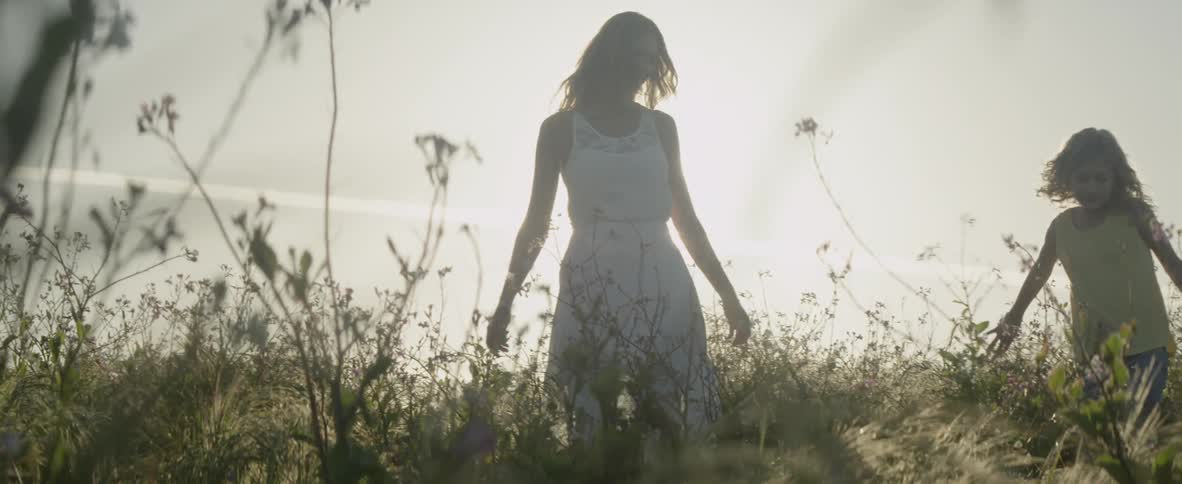 A woman and girl are walking through a field with flowers in daylight