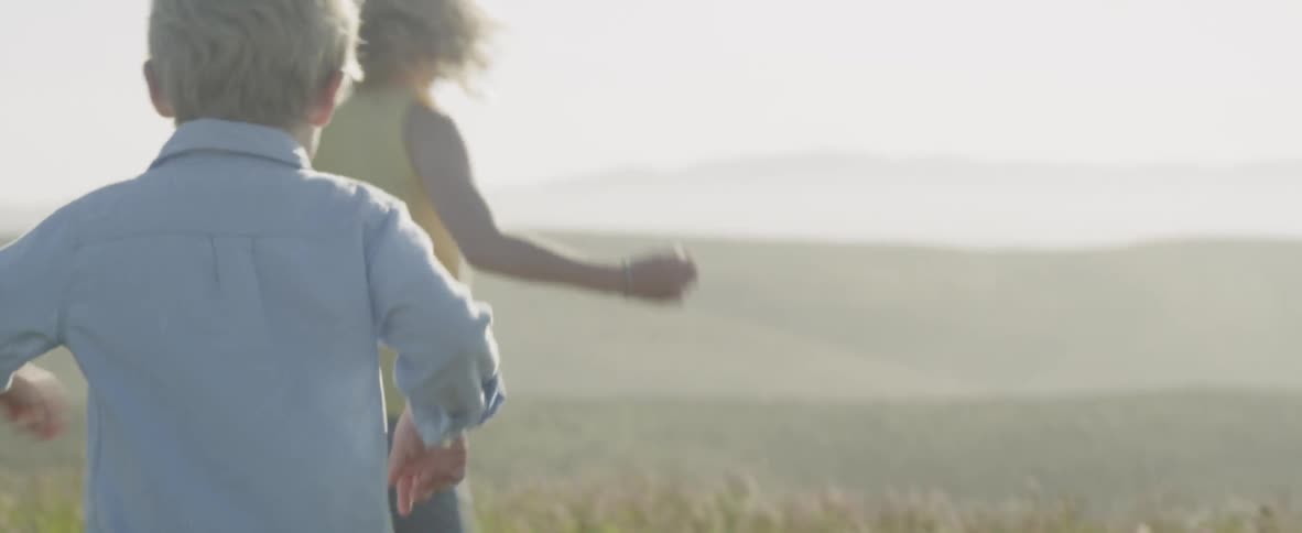 Young children running in a grassy area with clouds and hills in the background