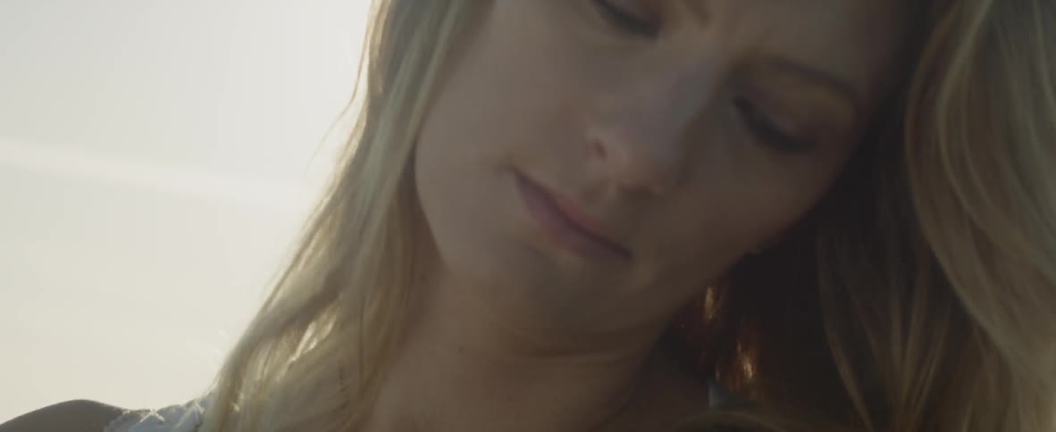 A woman stands outside with her eyes closed and the sun shining behind her