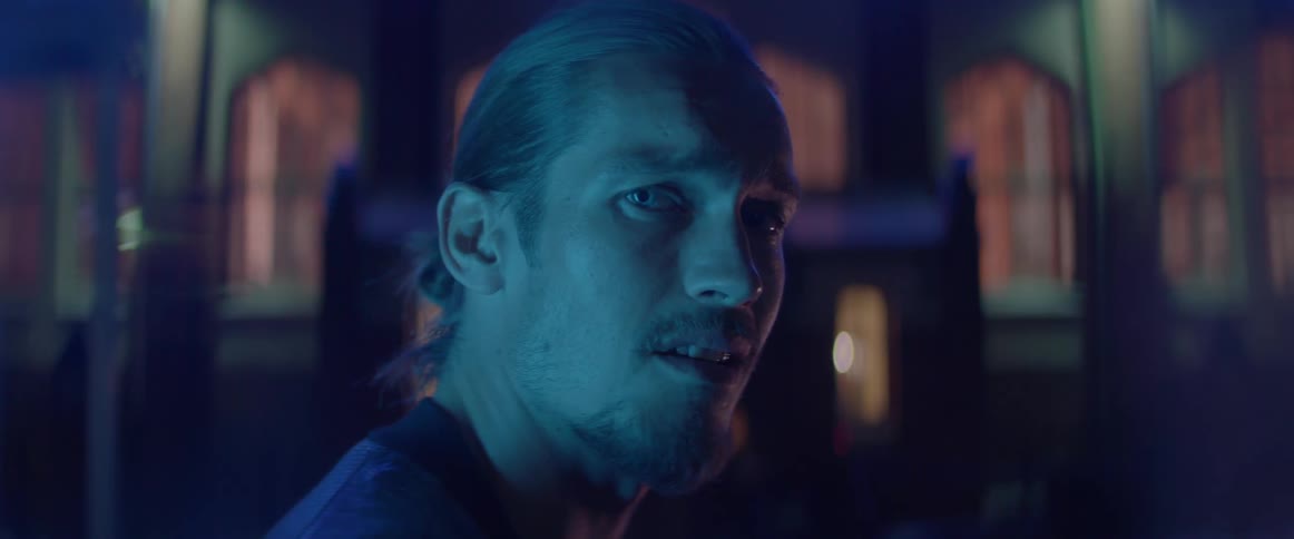 A bearded man looks over his shoulder with a mad expression at night.