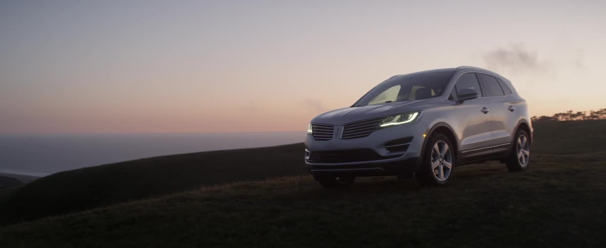 The silver car is parked on the hill at sunset