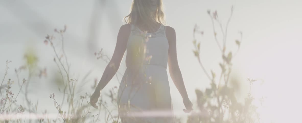 A woman walks through a grassy field on a sunny day