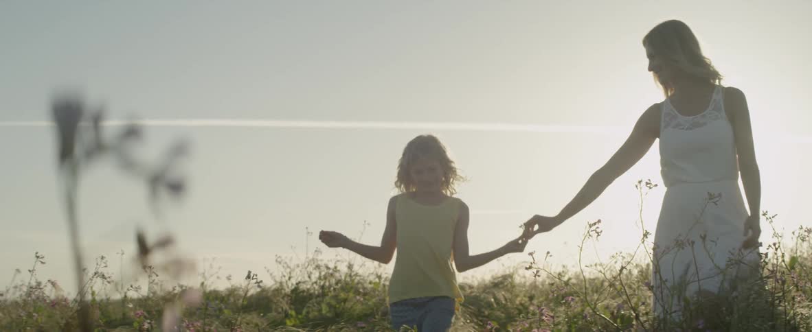 A woman and girl hold hands in a grassy field