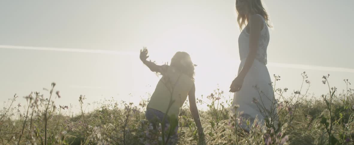 A woman and girl are walking through a field with flowers in daylight