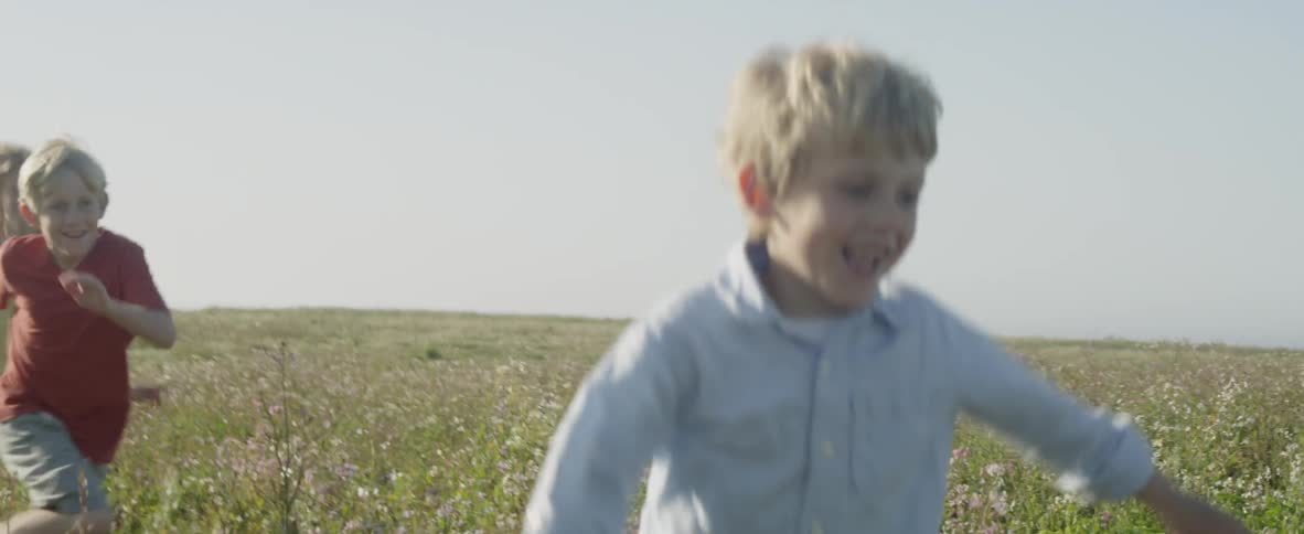 Young children smile and laugh as they run through tall grass and wildflowers