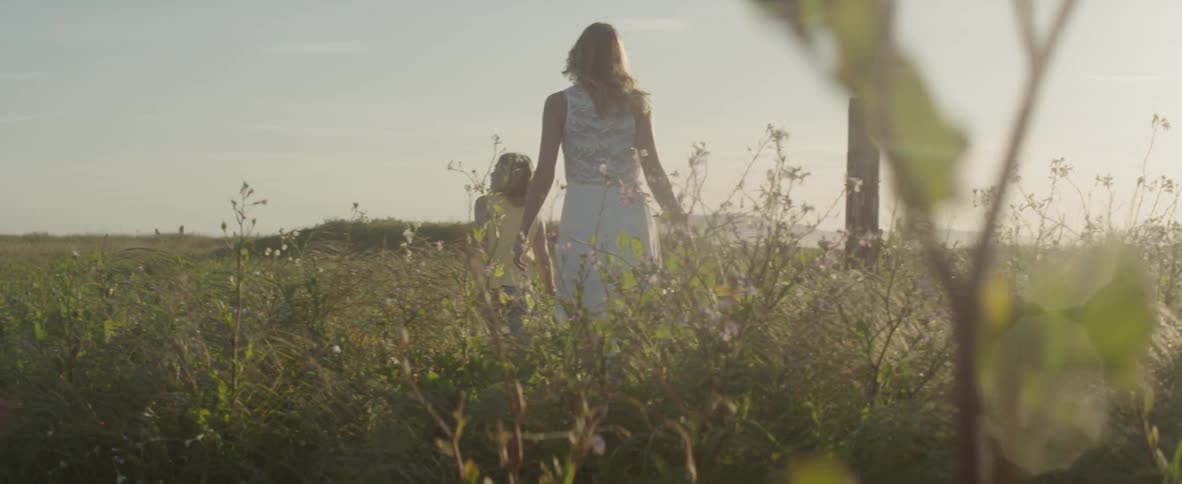 A woman and her daughter walk in a field on a sunny day