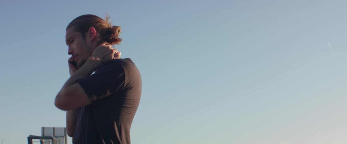 An anxious person covers his neck while pacing restlessly outside during the daytime.