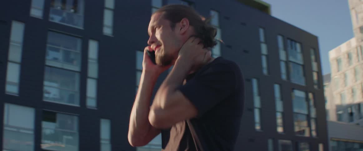 An anxious person massages his shoulders while talking on mobile phone during daytime.
