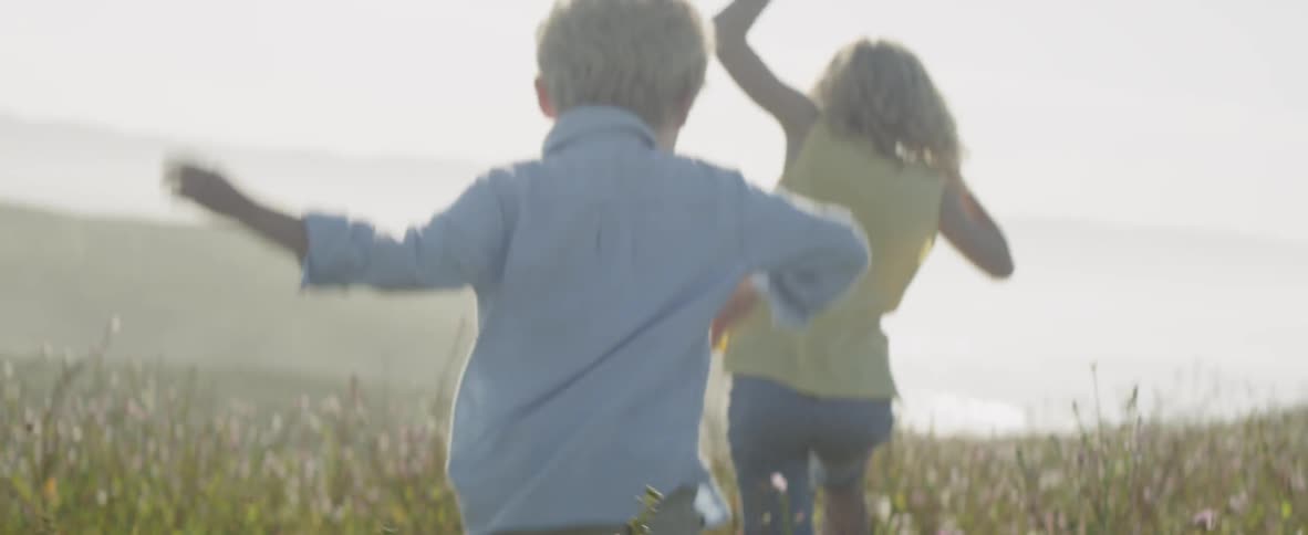A young boy and girl play in a grassy area with tall weeds
