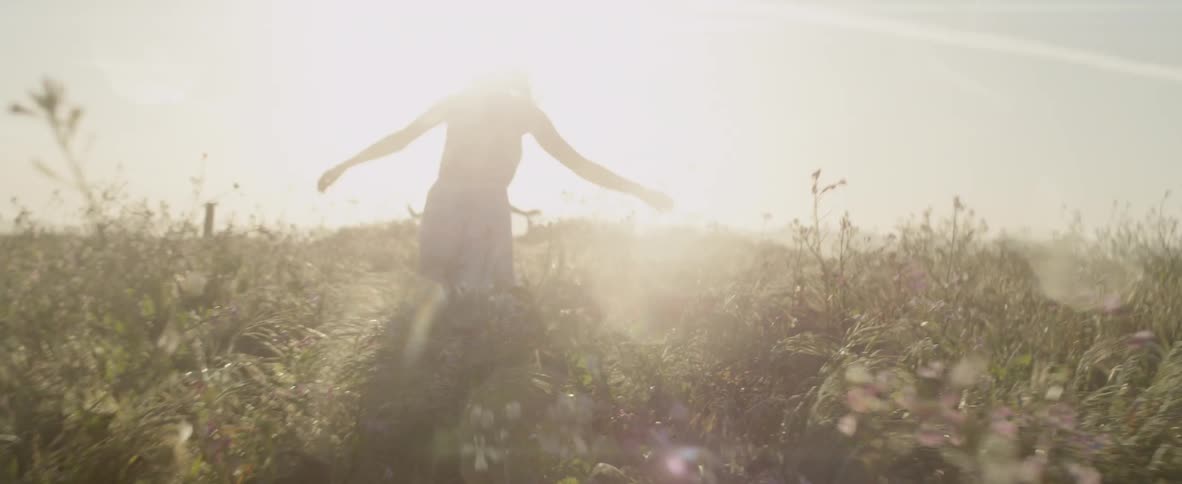 A woman and a child run through overgrown grass and weeds on a sunny day