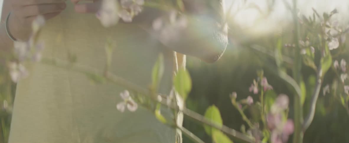 A girl is holding flowers in her hands as she stands outside in a field in daylight