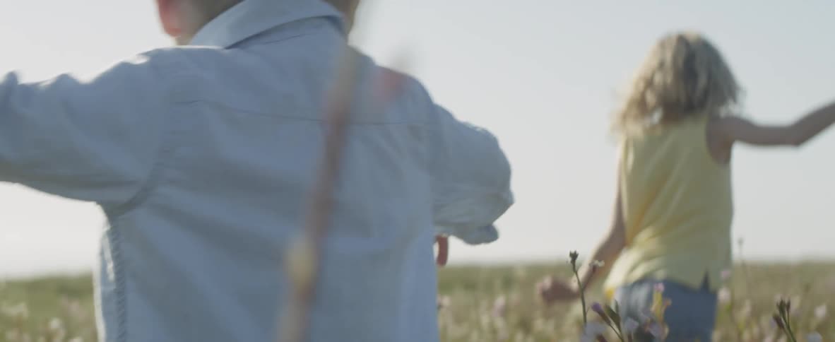 A young boy and girl running through an area with tall weeds and grass