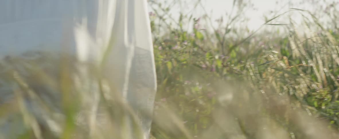 A woman walks through a grass field in a white dress