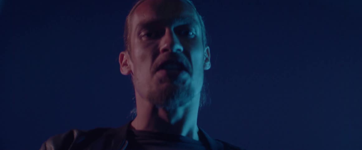 A furious young guy yells aggressively against a dark blue neon background outside.