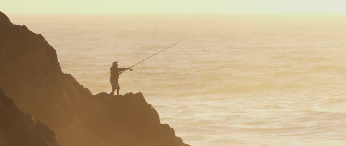 A man fishes from a rock on the coast
